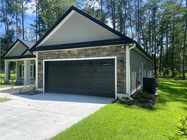 View of home's exterior featuring stone siding, concrete driveway, a lawn, and an attached garage | Image 4