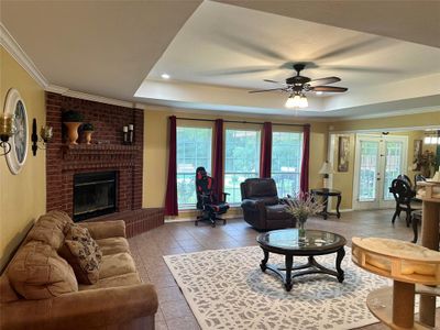 Tiled living room with a raised ceiling, ceiling fan, a fireplace, and ornamental molding | Image 3