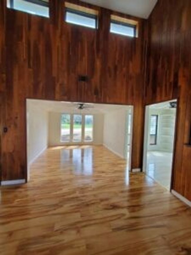 Unfurnished living room with a high ceiling, wooden walls, plenty of natural light, and wood finished floors | Image 8