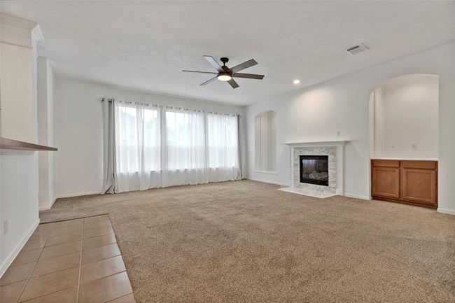 Spacious living room with neutral carpet, large windows, and natural light. Features a modern ceiling fan, a cozy fireplace with a white mantel, and built-in shelving. | Image 8