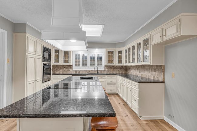 Kitchen with black appliances, a center island, a textured ceiling, backsplash, and light wood finished floors | Image 9
