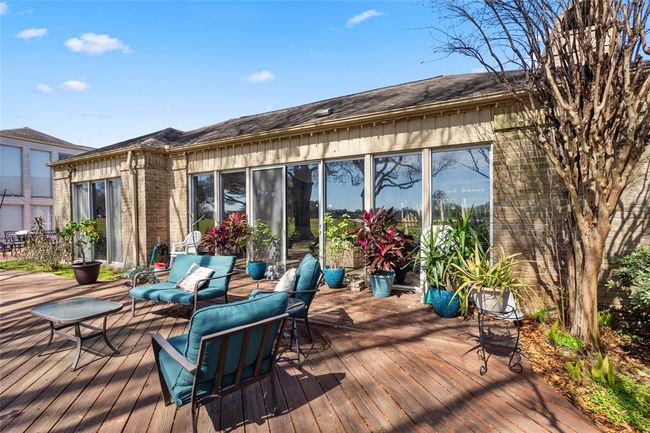 The expansive wooden deck offers a serene outdoor living space, seamlessly connecting to the home's interior through large sliding glass doors. Surrounded by lush greenery and mature trees, this area provides a perfect setting for relaxation or entertaining, with picturesque views of the golf course. | Image 36