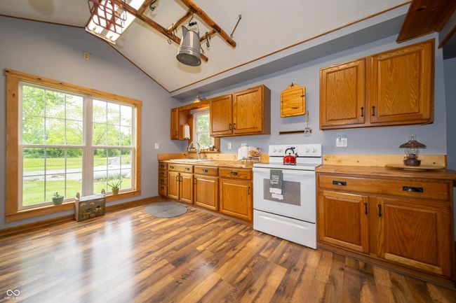 kitchen featuring white range with electric stovetop, brown cabinets, light countertops, lofted ceiling, and wood finished floors | Image 19