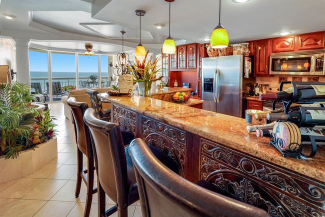 Kitchen featuring appliances with stainless steel finishes, light tile patterned floors, decorative light fixtures, decorative backsplash, and light stone countertops | Image 19
