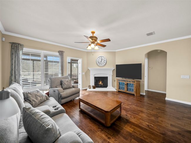 Living area with arched walkways, baseboards, dark wood-style floors, a glass covered fireplace, and crown molding | Image 15