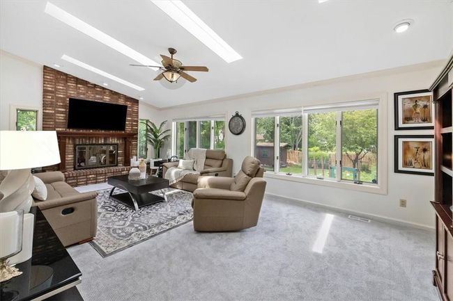 Carpeted living room featuring a healthy amount of sunlight, brick wall, lofted ceiling, and a fireplace | Image 10