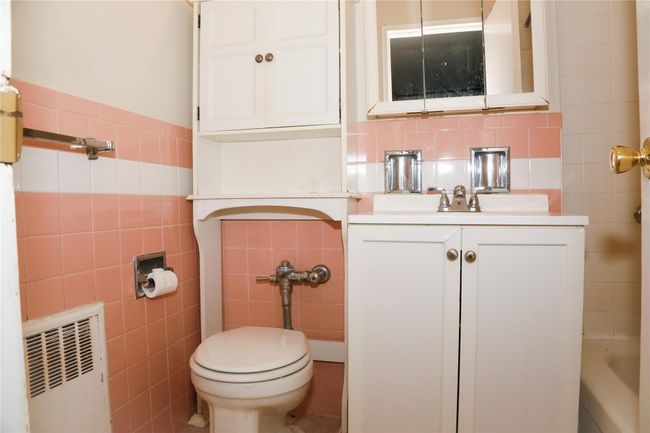Bathroom with tile walls, radiator heating unit, vanity, and toilet | Image 10