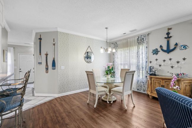 Dining space featuring a chandelier, ornamental molding, wallpapered walls, wood finished floors, and baseboards | Image 12