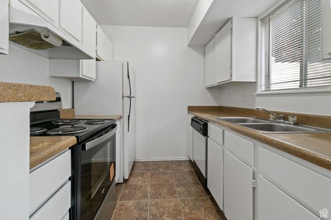 Kitchen featuring range with electric stovetop, white cabinetry, dishwasher, under cabinet range hood, and dark stone finish floors | Image 6