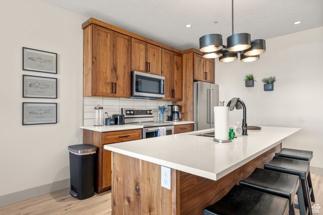 Kitchen with stainless steel appliances, light wood-style floors, brown cabinets, a sink, and recessed lighting | Image 58