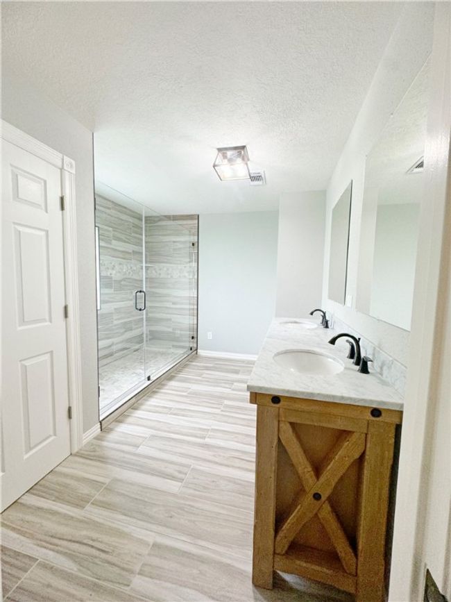 Full bath featuring a textured ceiling, a sink, double vanity, visible vents, and a shower stall | Image 5