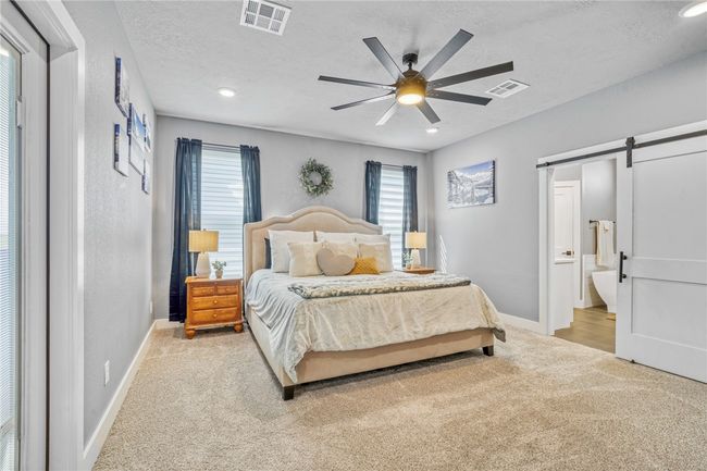 Carpeted bedroom with connected bathroom, a barn door, a textured ceiling, and ceiling fan | Image 22