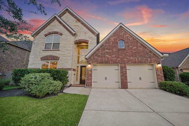 Charming two-story home with a brick and stone exterior, featuring a three-car garage. The well-maintained front yard has lush green grass and neatly trimmed bushes. | Image 37