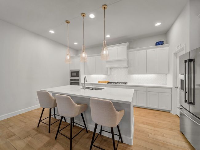 Kitchen featuring light wood-type flooring, appliances with stainless steel finishes, a kitchen breakfast bar, a kitchen island with sink, and recessed lighting | Image 8