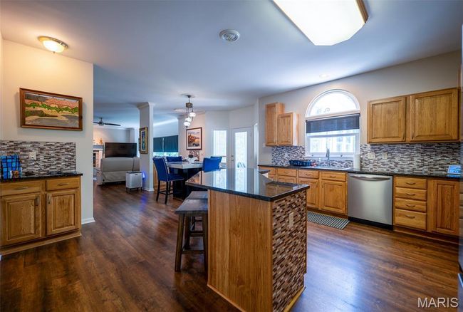 Kitchen featuring dishwasher, a ceiling fan, decorative backsplash, dark wood finished floors, and a kitchen breakfast bar | Image 9