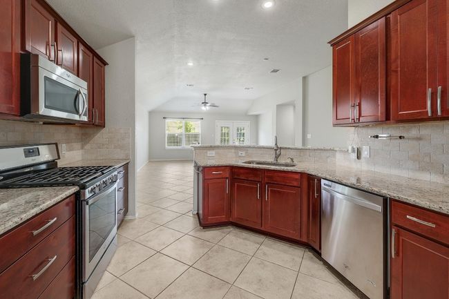 Kitchen featuring appliances with stainless steel finishes, dark brown cabinets, vaulted ceiling, a peninsula, and backsplash | Image 11