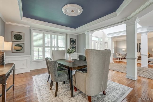 Elegant formal dining room featuring rich hardwood floors, detailed crown molding, classic wainscoting, a tray ceiling, and plantation shutters for timeless sophistication. | Image 12