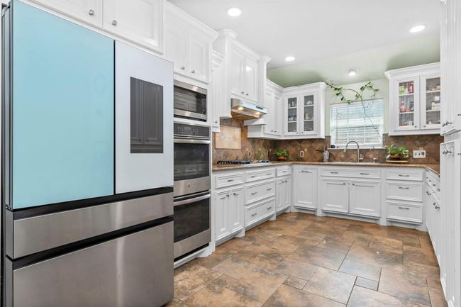 This is a modern kitchen featuring stainless steel appliances, white cabinetry, a tile backsplash, and tiled flooring, with ample natural light coming from multiple windows. | Image 21
