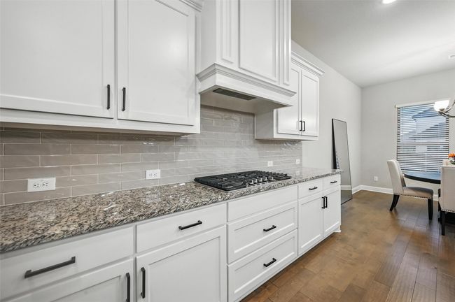 Kitchen featuring stainless steel gas cooktop, white cabinets, stone countertops, and backsplash | Image 17