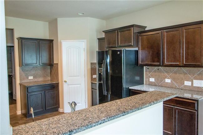 Kitchen featuring black fridge with ice dispenser, light stone countertops, dark brown cabinetry, decorative backsplash, and wood finished floors | Image 15