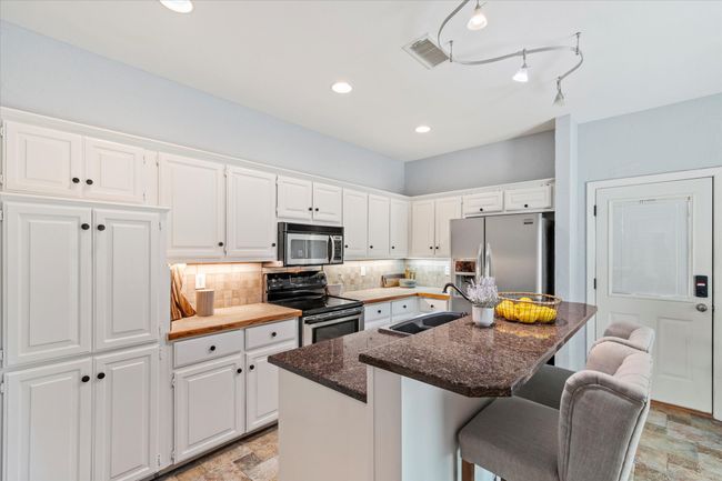 Kitchen featuring appliances with stainless steel finishes, a sink, backsplash, white cabinets, and a kitchen breakfast bar | Image 8