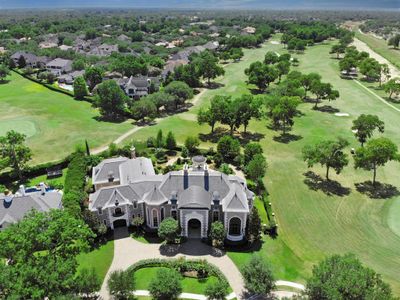 This is an aerial view of a large, luxurious estate with a grand residence featuring an expansive manicured lawn and direct access to a lush golf course. The home's architecture is elegant, with a symmetrical design and multiple gables. It's situated in a serene, green neighborhood. | Image 3