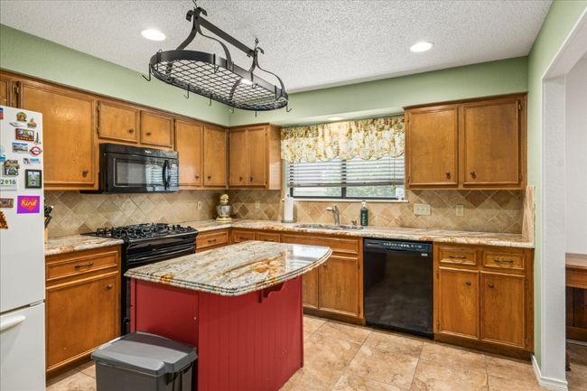 Kitchen with black appliances, brown cabinets, a textured ceiling, a kitchen island, and decorative backsplash | Image 15
