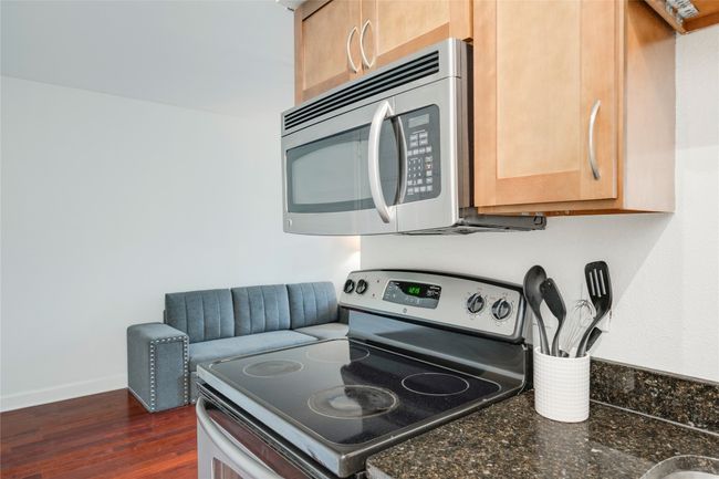 Kitchen with appliances with stainless steel finishes, dark wood-style floors, baseboards, dark stone countertops, and light brown cabinets | Image 16
