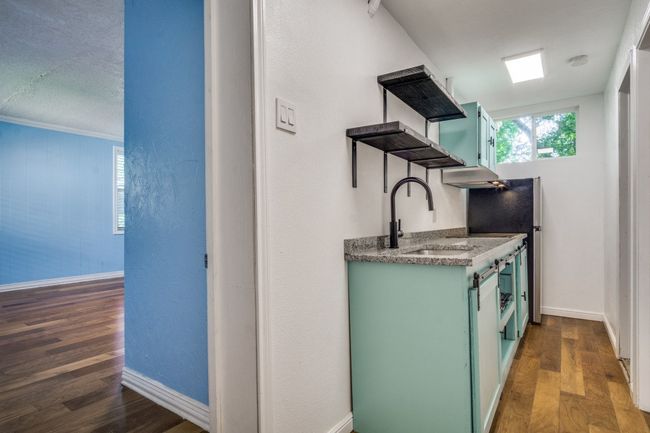 Kitchen with green cabinetry, open shelves, wood finished floors, and wall chimney range hood | Image 21