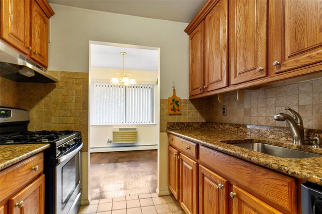 Kitchen with stainless steel gas range, a baseboard heating unit, brown cabinets, and under cabinet range hood | Image 14