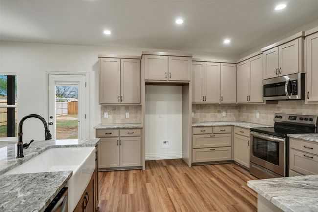 Kitchen with stainless steel appliances, a sink, tasteful backsplash, light wood-type flooring, and light stone counters | Image 11