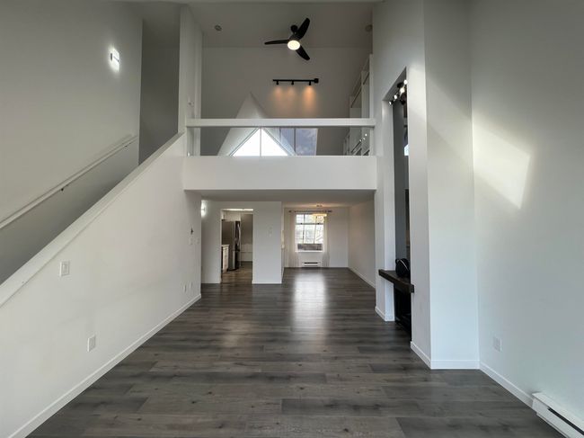 Unfurnished living room with a baseboard heating unit, wood finished floors, a high ceiling, and a barn door | Image 5
