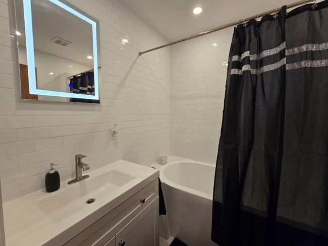 Full bath with visible vents, tile walls, shower / bathtub combination with curtain, vanity, and backsplash | Image 9