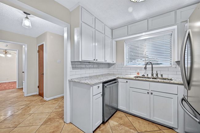 Kitchen featuring appliances with stainless steel finishes, decorative backsplash, a textured ceiling, light tile patterned flooring, and white cabinetry | Image 8
