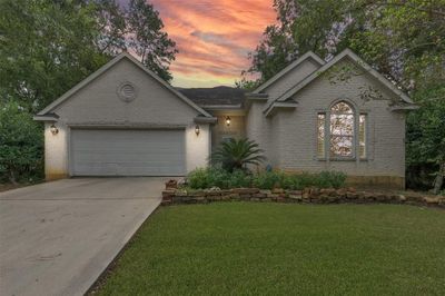 Enchanting single-story residence, boasting a classic brick facade with elegant gables and expansive windows, complemented by a spacious two-car garage and a pristine lawn, all framed by a stunning sunset. | Image 1