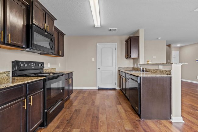 Kitchen featuring visible vents, a sink, black appliances, a peninsula, and dark wood-type flooring | Image 7