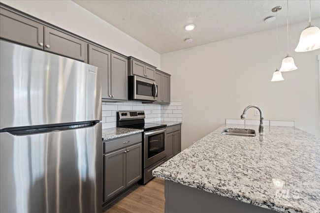 Kitchen with appliances with stainless steel finishes, light stone counters, hanging light fixtures, decorative backsplash, and dark wood-type flooring | Image 8