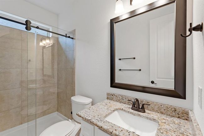 This stylish bathroom features a sleek shower/tub combo with a sliding glass door, complemented by a white sink vanity with a luxurious granite countertop! | Image 9