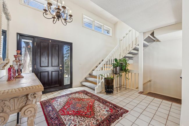 Welcoming foyer with a tiled floor, grand staircase, large window for natural light, and double front doors offering a warm and elegant entry point to the home. | Image 12