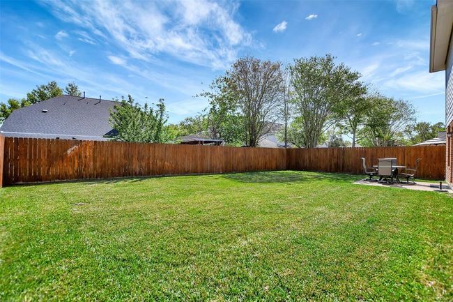 Spacious backyard with a well-maintained lawn and a wooden privacy fence. There's a small patio area with outdoor furniture, ideal for relaxation or entertaining. | Image 43