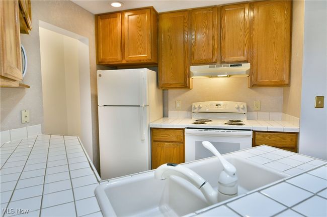 Kitchen with white appliances, under cabinet range hood, tile countertops, and brown cabinets | Image 9