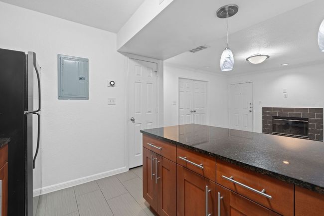 Kitchen featuring visible vents, electric panel, freestanding refrigerator, dark stone counters, and hanging light fixtures | Image 18