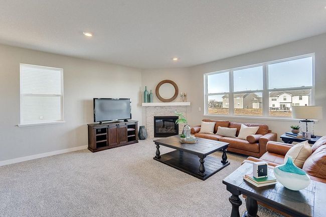 Punctuated by this corner gas fireplace, the home's main level family room is coated in hard surface flooring and is flooded in natural light via soaring windows overlooking the backyard! Photo of model home, color and options will vary. | Image 9