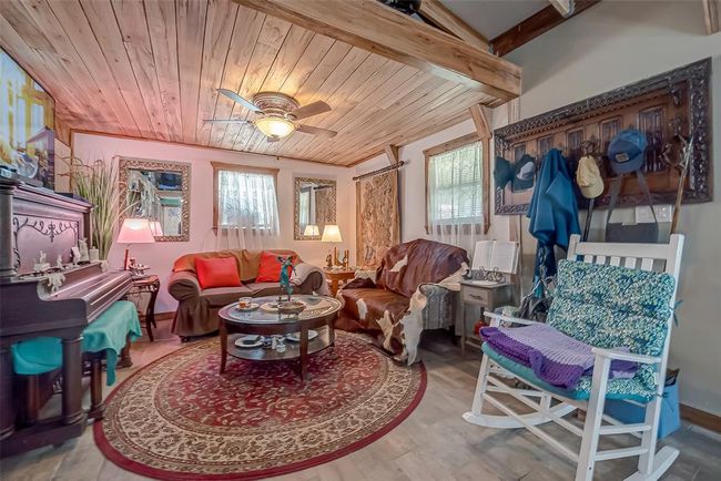 The living space offers an intimate setting, with warm ceiling details and soft light filtering through the windows. A ceiling fan keeps things breezy, while the layout remains grounded in comfort. | Image 16