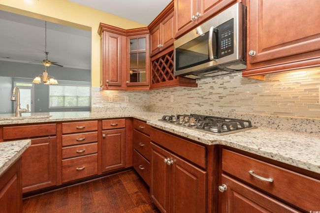 Kitchen featuring a sink, decorative backsplash, dark wood-type flooring, light stone counters, and appliances with stainless steel finishes | Image 8
