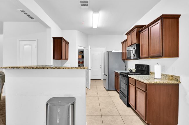 Kitchen with light tile patterned flooring, light stone counters, visible vents, and black appliances | Image 11