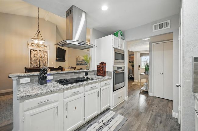 Kitchen featuring appliances with stainless steel finishes, island range hood, a peninsula, wood finished floors, and white cabinetry | Image 13