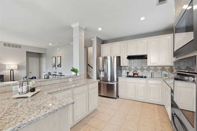 * Virtual rendering of kitchen cabinets painted white. Kitchen featuring stainless steel fridge, black oven, light tile patterned floors, decorative backsplash, and light stone counters | Image 4