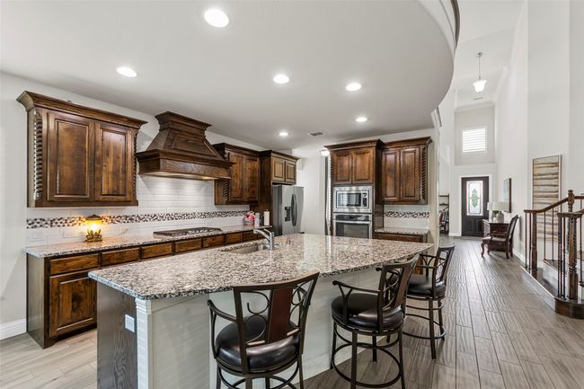 Kitchen featuring stainless steel appliances, a sink, wall chimney exhaust hood, backsplash, and a breakfast bar area | Image 10