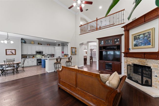 Living room featuring arched walkways, ceiling fan, ornamental molding, wood finished floors, and a stone fireplace | Image 6
